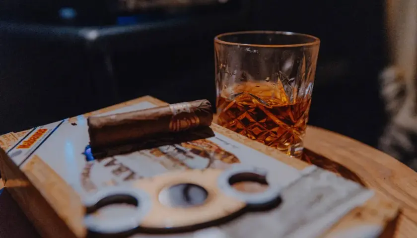 Un verre de whisky ambré et un cigare posés sur une boîte de cigares, prêts pour un moment de détente.