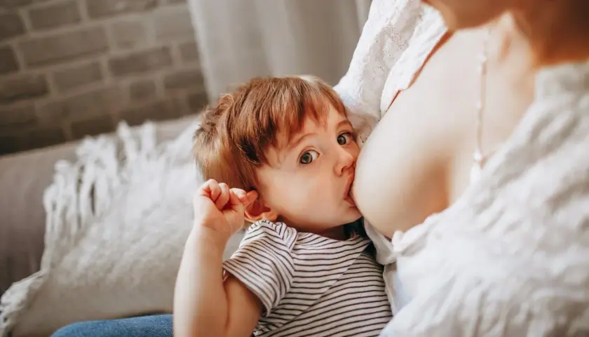 Un bimbo con occhi grandi e curiosi viene allattato dalla mamma. Un momento intimo, un gesto naturale, un esempio di allattare in pubblico senza timori.