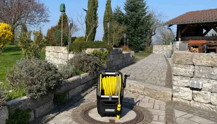 Ein gelber Schlauchwagen steht auf einem gepflasterten Weg im Garten, bereit für die Gartenarbeit.