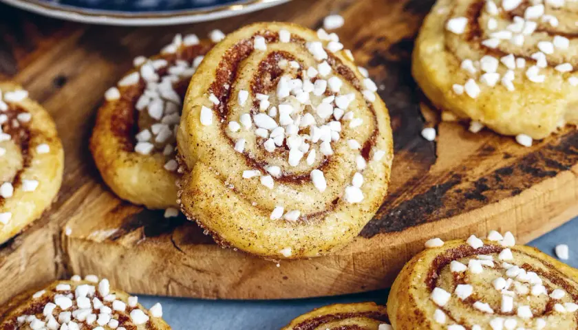 Nybakade kanelbulle kakor med pärlsocker på en träskärbräda. Perfekt fika!