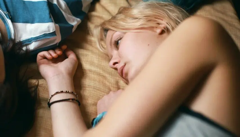 Två unga kvinnor ligger nära varandra, en med blont hår och en med mörkt. En scen som påminner om svenska ungdomsfilmer från 90-talet.