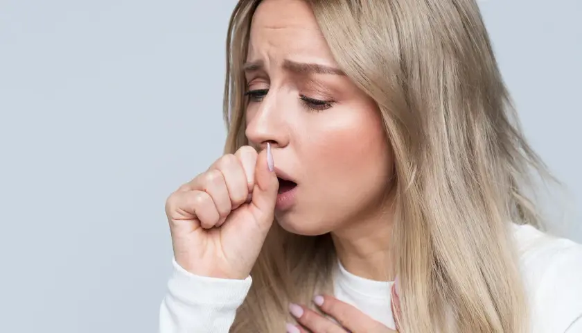 Mujer rubia con expresión de malestar, tosiendo y sujetándose el pecho. Sufre dolor en el pecho al toser sin fiebre.