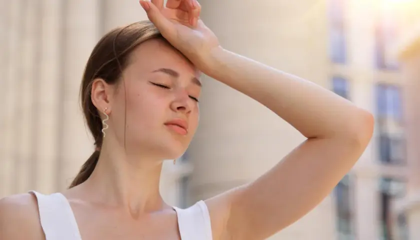 Une jeune femme essuie sa sueur sous un soleil de plomb, se demandant combien de temps dure un coup de chaleur.