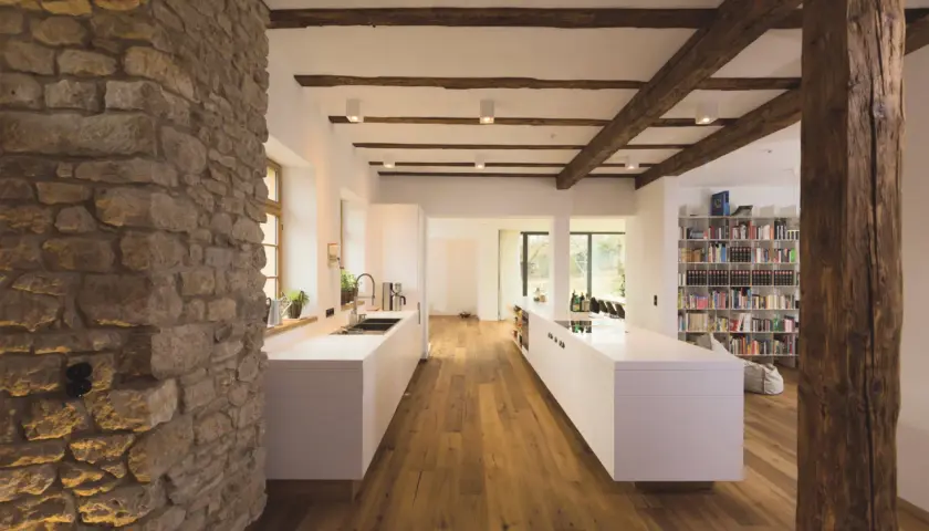 Modernes Wohnen mit Fachwerk: Eine Küche mit weißen Inseln und Holzbalken, die das Fachwerk innen gestalten.