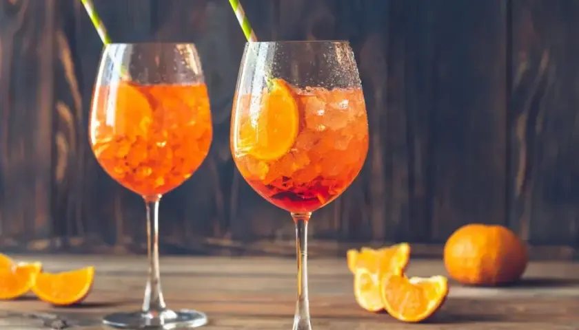 Dwa orzeźwiające drinki Aperol z pomarańczą i słomkami, na drewnianym stole.