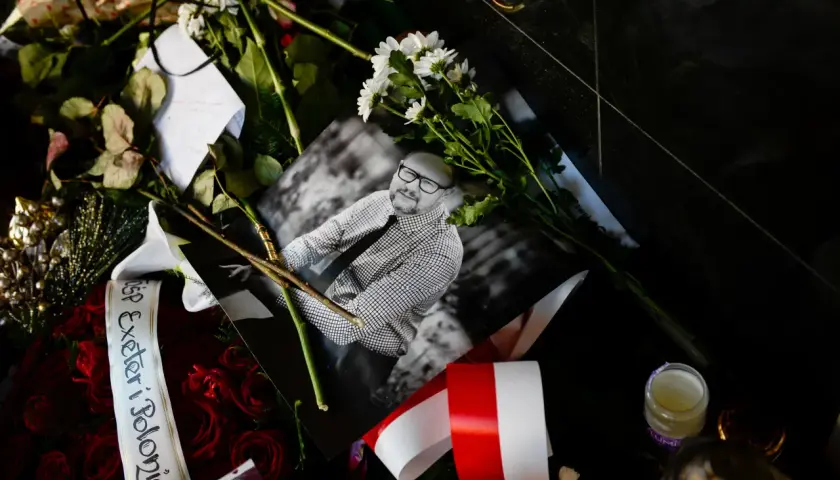 Czarne tło, bukiety czerwonych róż, białe kwiaty, zdjęcie mężczyzny w okularach, polska flaga. W tym miejscu panuje cisza.