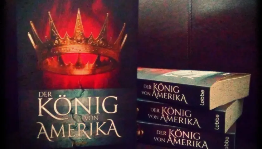 Michael Peinkofer präsentiert "Der König von Amerika". Ein Buchcover mit Krone und gestapelte Exemplare des Romans.