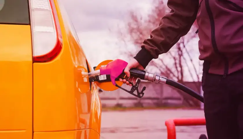 Mano con guanto rosa inserisce la pompa di benzina nel serbatoio di un'auto arancione. Il **consumo auto** è una spesa da considerare.