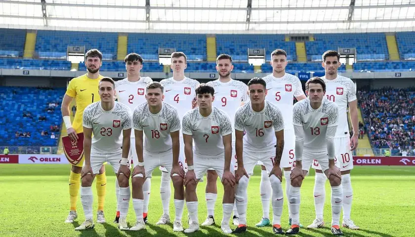 Młodzieżowa reprezentacja Polski w piłce nożnej pozuje do zdjęcia na stadionie.