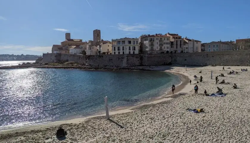 Sonniger nizza strand mit Menschen, die sich entspannen, und einer historischen Stadt im Hintergrund.