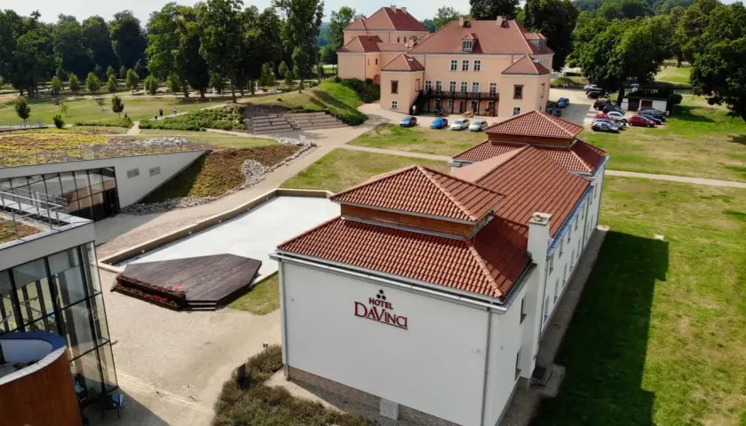 Widok z lotu ptaka na Hotel Da Vinci z czerwonym dachem, otoczony zielenią i innymi budynkami.