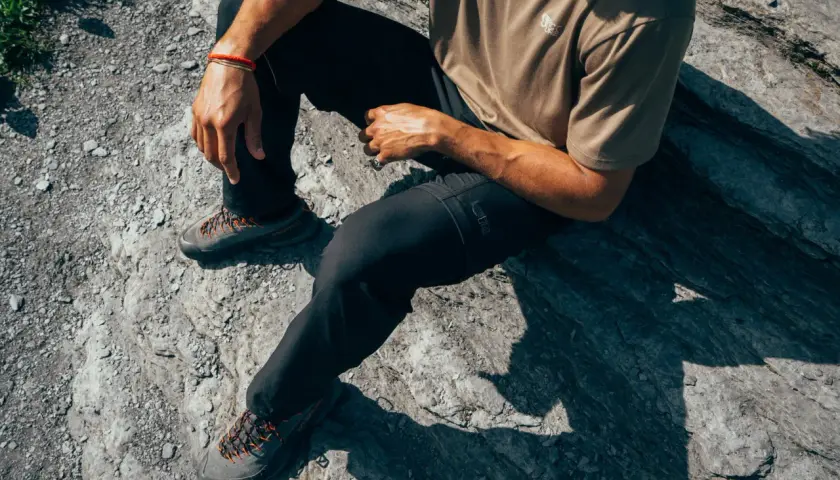 Man sitting on rocks, wearing black pants and hiking shoes. The shoes are grey with orange laces, perfect for schoenen oprekken on any terrain.