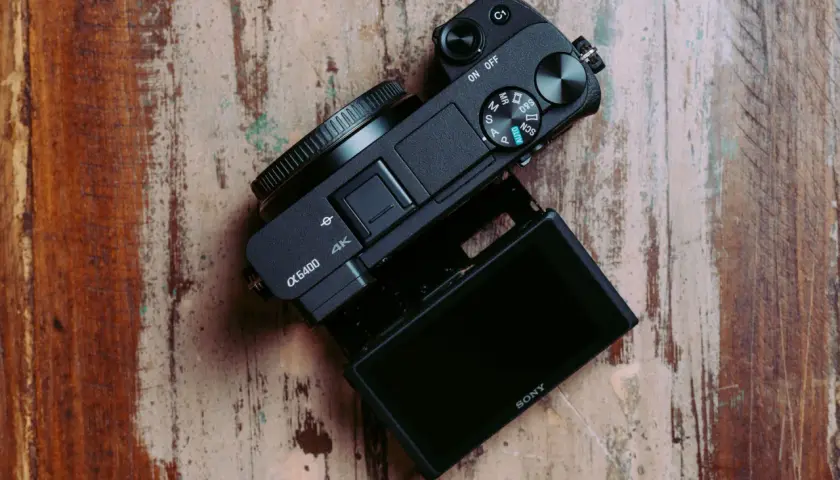Czarny aparat Sony α6400 z uchylnym ekranem leży na drewnianym blacie. Idealny do testów i vlogowania.