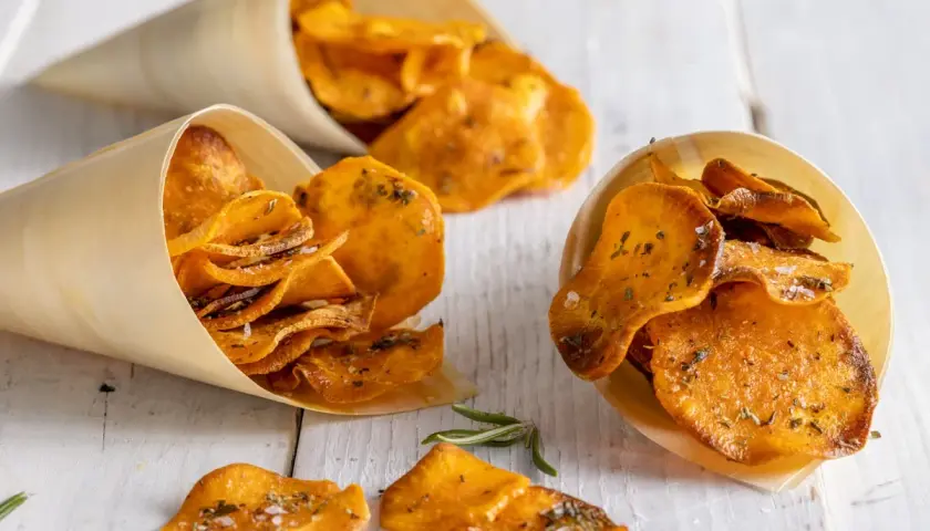 Croccanti patate dolci in padella, condite con erbe aromatiche e sale, servite in coni di legno.