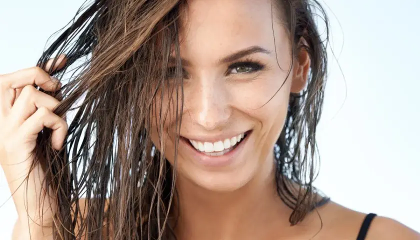 Mujer sonríe con pelo efecto mojado, luciendo natural y radiante.