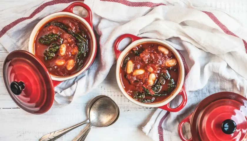 Due ciotole rosse con zuppa di cavolo nero e fagioli, pronte per essere gustate.