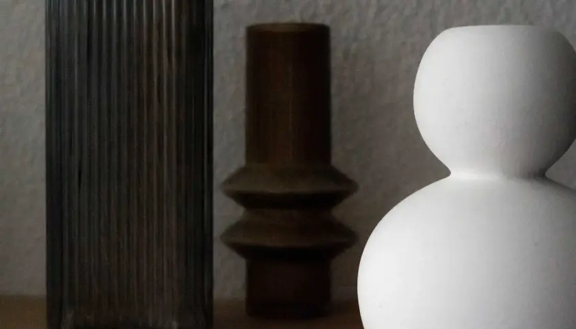 Drei Vasen in verschiedenen Formen und Farben: eine hohe, geriffelte dunkle, eine braune mit zwei Wölbungen und eine weiße, kugelförmige. Perfekt zum Vase dekorieren ohne Blumen.