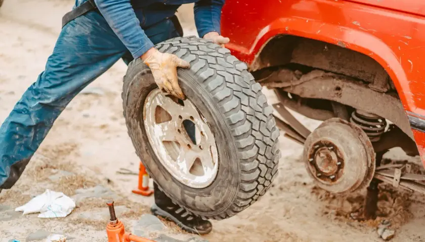 Persona con guanti smonta una gomma auto da un fuoristrada rosso. Si vede un cric arancione a terra, utile per capire dove smaltire gomme auto usate.