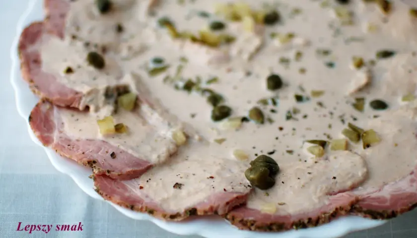 Cienkie plastry pieczonego mięsa wieprzowego polane kremowym sosem z kaparami i ziołami, klasyczne vitello tonnato.