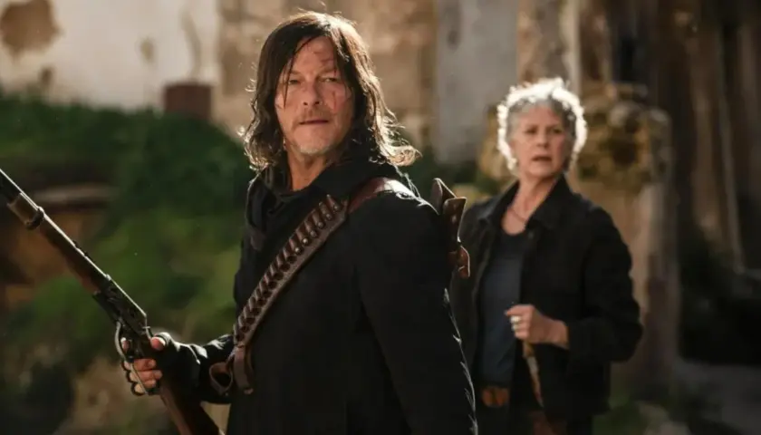 Daryl i Carol, bohaterowie seriali o zombie, przygotowują się do walki. Daryl trzyma strzelbę, a Carol stoi za nim.