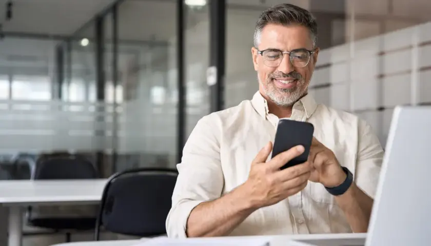 Uśmiechnięty mężczyzna z telefonem w dłoni, szukający informacji, jak udostępnić internet z telefonu na laptopa.