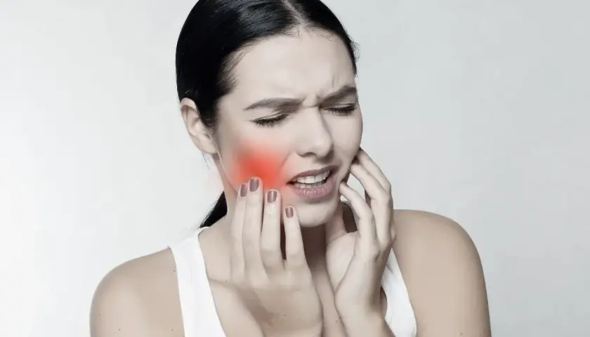 Mujer con dolor, tocándose la mejilla donde se ve un bulto mejilla interna enrojecido.