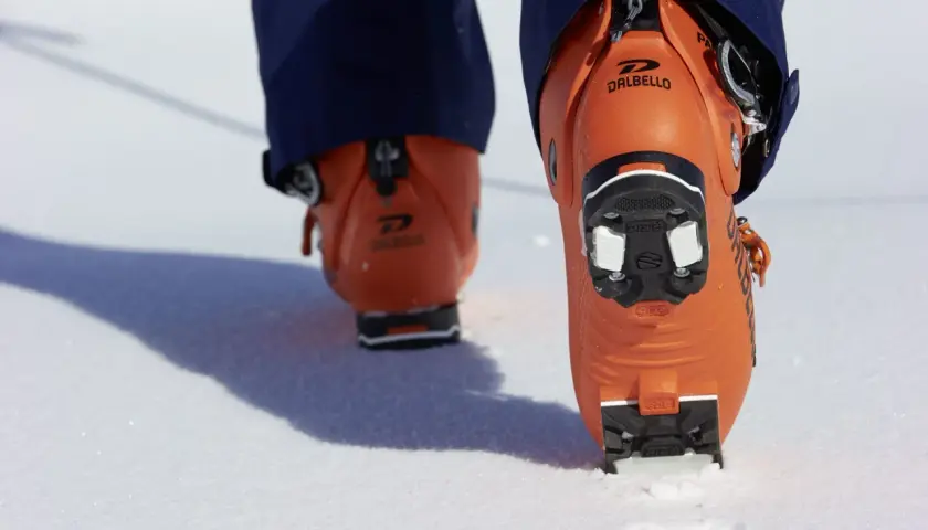 Botas de esquí naranjas Dalbello con suela de **grip walk** en la nieve, listas para la aventura.