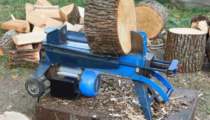 Ein Holzspalter mit einem dicken Holzstamm, bereit, dickes Holz zu spalten. Daneben liegen bereits gespaltene Holzscheite.