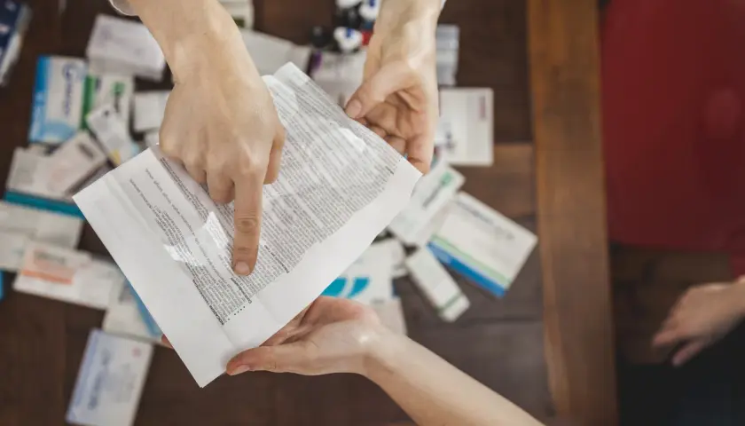 Mani che consultano un foglietto illustrativo tra scatole di medicinali, spiegando il significato di "off label" per un uso non previsto.
