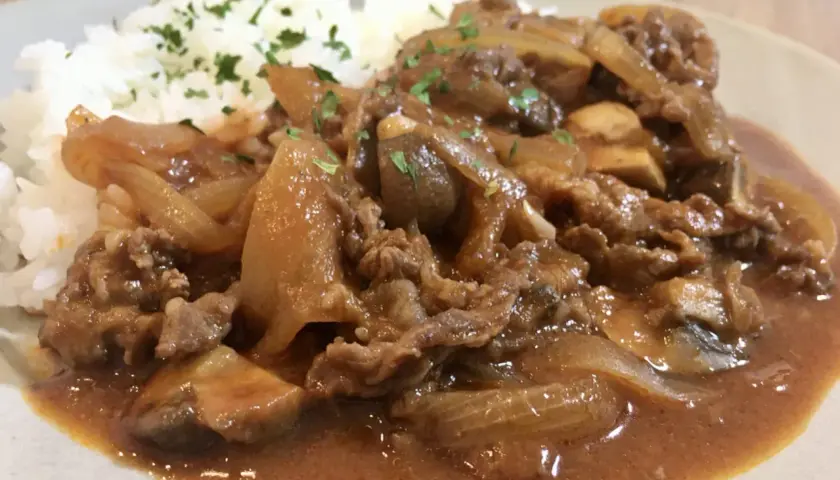 A plate of Hayashi Rice, featuring tender beef and onions in a rich demi-glace sauce served over fluffy white rice, garnished with parsley.