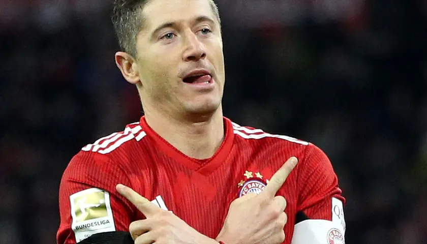 Robert Lewandowski w czerwonej koszulce Bayernu z naszywką Bundesligi, wykonuje gest radości po strzelonej bramce.