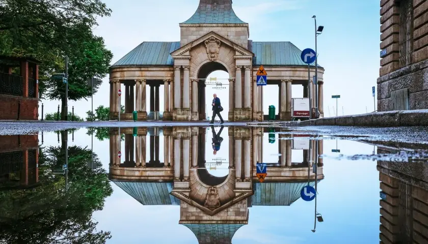 Odbicie zabytkowego budynku z kolumnami w kałuży po deszczu.