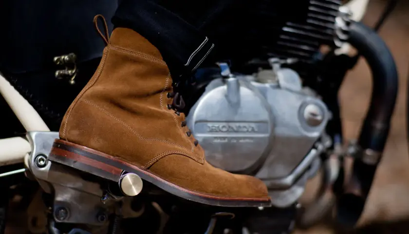 A suede boot rests on a motorcycle engine, ready for a ride. Learn how to walk in boots like these for style and comfort.
