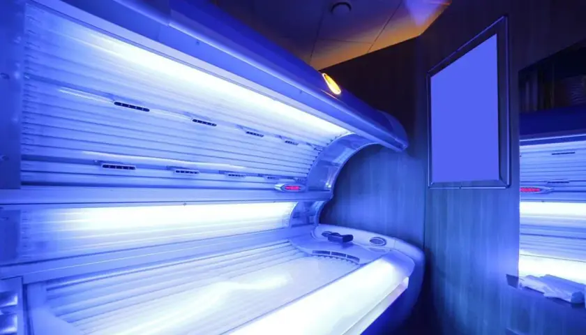 Wnętrze solarium z łóżkiem do opalania. Jasne lampy emitują niebieskie światło, tworząc atmosferę relaksu i przygotowania do letniego okresu.