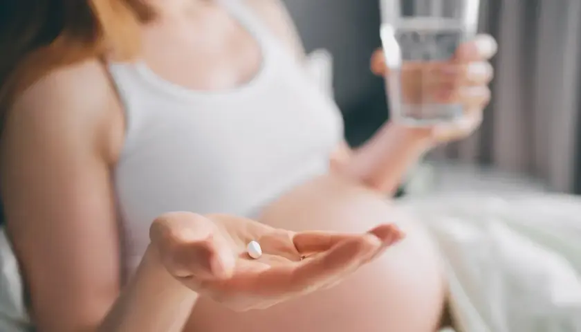 Kobieta w ciąży bierze tabletkę i popija ją wodą, dbając o prawidłowe ciśnienie w ciąży.