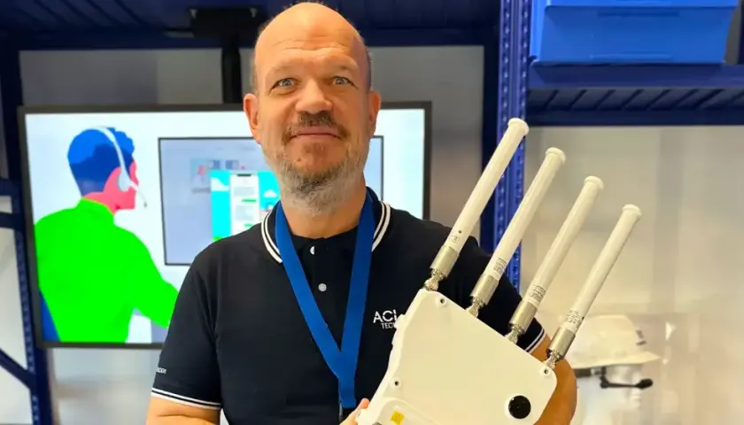 Un homme souriant tient un appareil avec quatre antennes, prêt à optimiser votre reseau wifi.