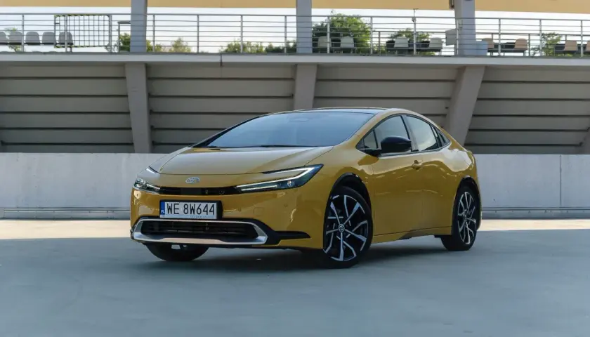 Nowy żółty Toyota Prius z nowoczesnym designem stoi na betonowym placu przed trybunami stadionu.