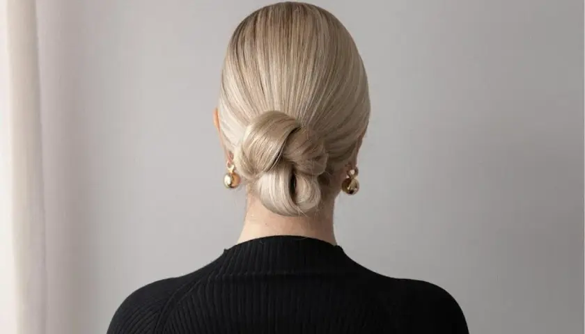 Elegancki kok z blond włosów, idealny na proste fryzury ślubne. Złote kolczyki dodają blasku.