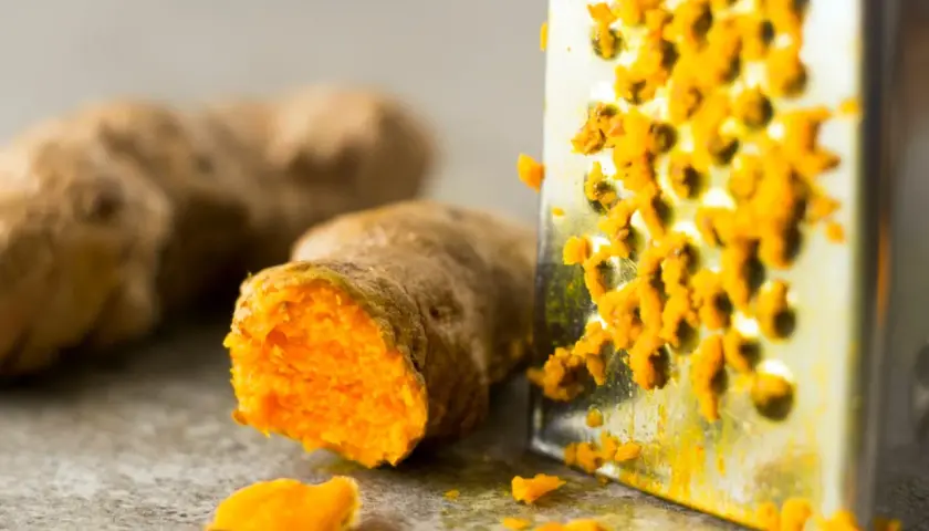 Frisch geriebene Kurkuma auf einem Metallreibe. So lässt sich die leuchtend orangefarbene Wurzel für die Lagerung vorbereiten.