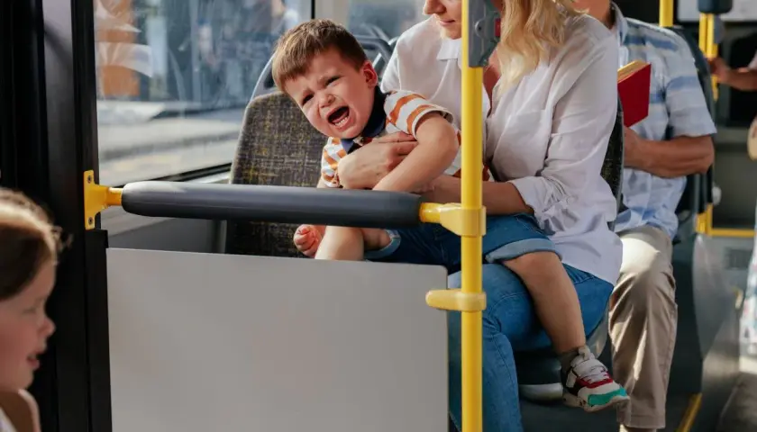 Płaczące dziecko na rękach matki w autobusie, obok siedzi starszy mężczyzna.