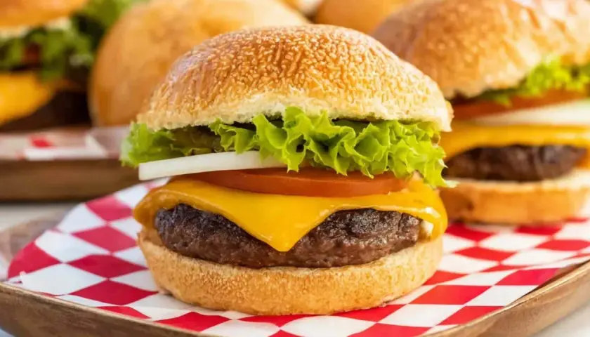 Soczyste mięso na burgery z serem, sałatą, pomidorem i cebulą, podane na kratkowanej serwetce.