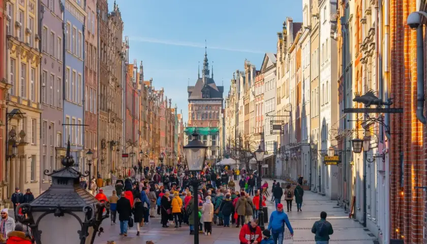 Tłum ludzi spaceruje ulicą Długą na gdańskiej starówce, podziwiając kolorowe kamienice i zabytkową architekturę.