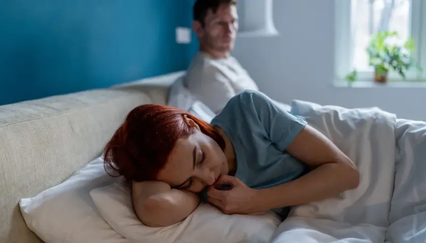 Kobieta z rudymi włosami śpi, czuje się zaniedbywana w związku. Mężczyzna siedzi z tyłu, odwrócony.