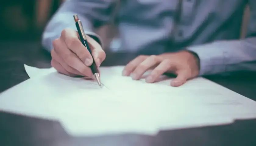 Dłoń pisze piórem na papierze, ćwicząc zwroty do maila po angielsku.