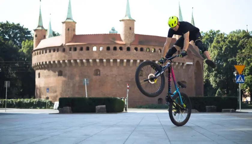 Rowerzysta wykonuje trik na tle Barbakanu. Odkryj **szlaki rowerowe Kraków** i poczuj wolność!