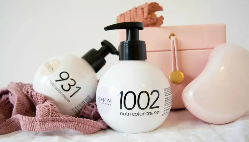 Två flaskor Revlon hårfärg, Nutri Color Creme, står framför en rosa smyckeskrin och en rosa tygbit.
