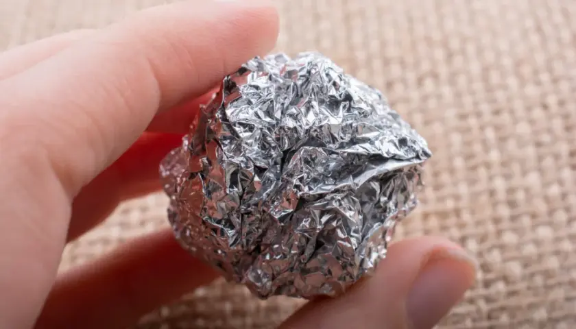 Dłoń trzyma kulkę z pogniecionej folii aluminiowej, która może być szkodliwa.