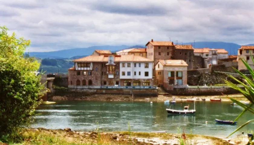 Pueblos de Cantabria con playa, casas de piedra y tejados rojos junto a un río tranquilo con barcas.