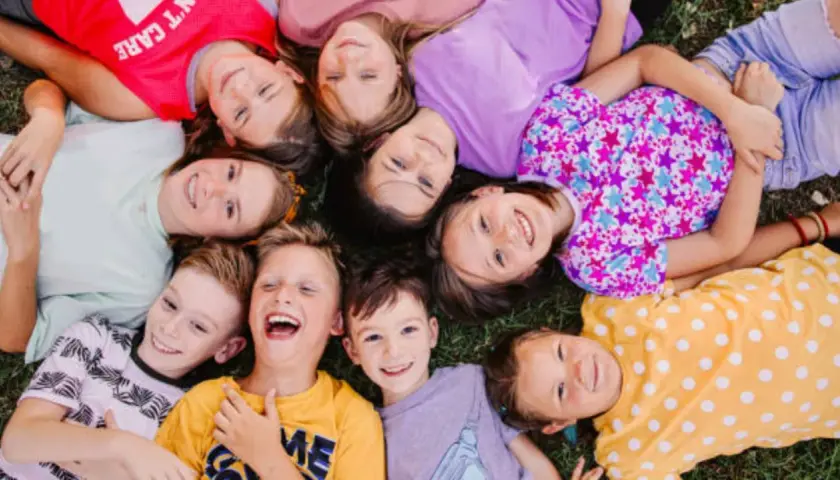 Niños sonriendo y jugando juntos en la hierba, una escena alegre de escuela de verano para niños de 2 años.