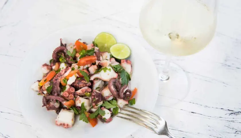 Frischer oktopus salat mit Tomaten, Petersilie und Limette, daneben ein Glas Weißwein.